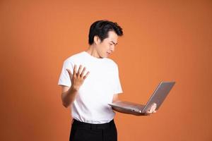 Aziatisch Mens Holding laptop, geïsoleerd Aan oranje achtergrond foto