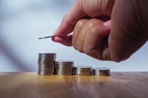 Mens hand- zetten geld naar munten stack Aan houten tafel met wazig achtergrond besparing concept foto