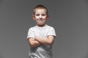 portret van gelukkig weinig jongen in wit t-shirt glimlachen Aan grijs achtergrond op zoek Bij camera in studio instelling. portret van modieus mannetje kind. foto