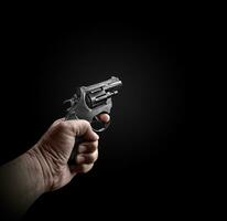 mannetje hand- Holding een zwart revolver Aan een zwart achtergrond criminelen met pistolen Bij dichtbij reeks wapens voor aanval of verdediging foto
