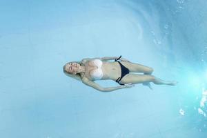 aantrekkelijk jong vrouw drijvend in een zwemmen zwembad met haar armen uitgestrekt, op zoek Bij de lucht foto