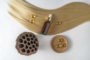 een haar- zorg olie of serum in een bruin druppelaar fles en gouden capsules aan het liegen Aan een blond haar- strand, Product afzet mockup foto