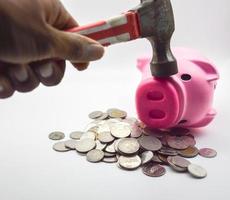 een stapel van roze varken munten aan het liegen Aan top een hand- Holding een hamer is beukende een roze varken. de concept van economisch depressie. inflatie, verlies foto