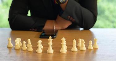 zakenman handen in zwart suite zittend en richten schaak koning Aan wijnoogst tafel betekenis van planning en strategie. besluit en prestatie doel concept. foto