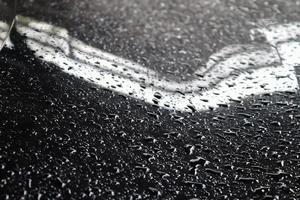 regendruppels op een zwart metalen auto-oppervlak in een close-upweergave. foto
