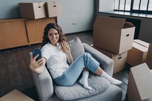 meisje blogger met telefoon golvend hand- groet volgers Aan verhuizing dag naar nieuw huis. in beweging, reparatie foto