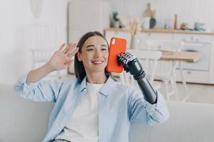 glimlachen gehandicapt meisje beantwoorden video telefoongesprek, Holding smartphone, gebruik makend van bionisch robot prothetisch arm foto