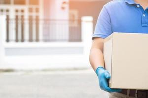 pakket levering Mens slijtage beschermend handschoenen blauw, beschermen hygiëne kiemen en bacterie van een pakket door een onderhoud sturen naar huis. hand- Holding verzenden en inzending klant accepteren een van doos. foto