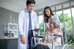 Aziatisch dokter uitleggen ziekte naar senior geduldig met tablet glimlachen in comfort Bij huis, gezondheidszorg en geneeskunde concept. foto