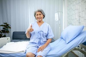 een ouderen vrouw duimen omhoog en glimlachen in de herstel kamer. gezondheidszorg en geneeskunde concept. foto