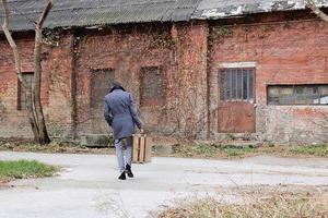 achterzijde visie van een Mens met koffer wandelen weg. foto