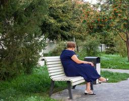 een vrouw is zittend met een telefoon Aan een park bank. foto