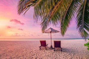 perfect tropisch zonsondergang landschap, twee zon bedden, ligstoelen, paraplu onder palm boom. wit zand, zee visie met horizon, kleurrijk schemering lucht, rust en ontspanning. inspirerend strand toevlucht hotel foto