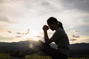 silhouet van christen vrouw bidden aanbidden Bij zonsondergang. christen religie concept achtergrond. handen in gebed. aanbidden god met religie concept. foto