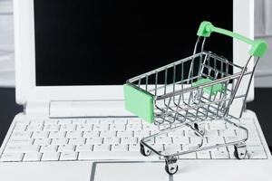 online uitverkoop en zwart vrijdag concept. laptop en mini boodschappen doen kar Aan wit achtergrond. foto