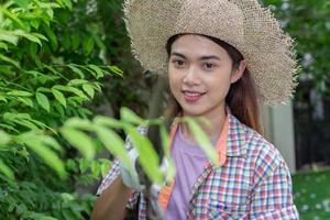 Aziatisch vrouw slijtage hoed snoeien struiken met groot tuin schaar. foto