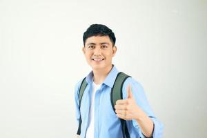 portret van een glimlachen mannetje leerling met rugzak tonen duimen omhoog over- wit achtergrond foto