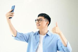 vrolijk jong Mens is maken selfie Aan de camera van zijn telefoon en tonen duim omhoog foto