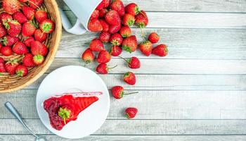 top visie van vers aardbei taart plakjes Aan een bord en vers rood aardbeien fruit Aan een blauw oud houten achtergrond foto