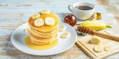 stack van banaan pannekoeken met plakjes van vers bananen, een zoet eigengemaakt stack van pannekoeken met boter en siroop voor ontbijt in houten achtergrond foto