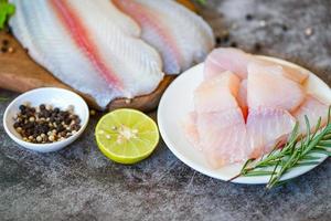 vers rauw pangasius vis filet met kruid en specerijen citroen limoen en rozemarijn, vlees dolly vis tilapia gestreept meerval, vis filet Aan wit bord met ingrediënten voor Koken foto