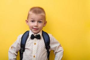 terug naar school. een blond grappig jongen met een rugzak in een licht overhemd Aan een geel achtergrond looks Bij de camera. kopiëren ruimte. onderwijs. foto