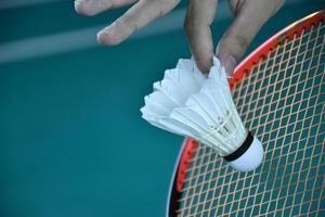 badminton speler houdt racket en wit room shuttle in voorkant van de netto voordat portie het naar een ander kant van de rechtbank. foto