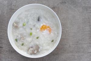 top visie van rijst- pap of congee met ei in wit kom Aan wijnoogst houten tafel achtergrond. foto