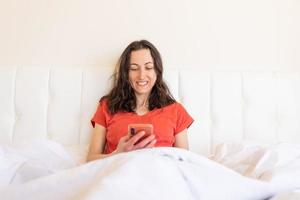 een vrouw zit op een bed en houdt een smartphone in haar handen foto