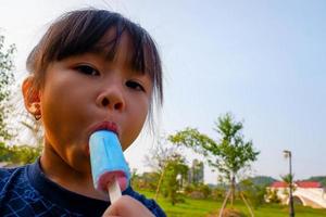 close-up portret van de mooie, schattige, kleine dame, ijs etend in watermeloen in haar mond, met hartpoort en blauwe hemelachtergrond. foto