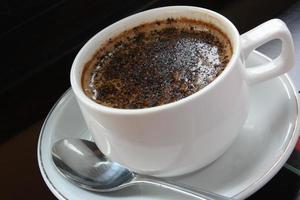een kopje warme chocolademelk espressokoffie. met chocoladehagelslag. witte kop en schotel. een roestvrijstalen lepel. zwarte achtergrond. close-up bovenaanzicht. foto