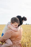 gelukkige familie van moeder en baby kind lopen op tarweveld, knuffelen en zoenen foto