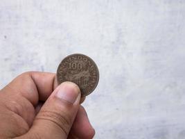 een Mens Holding een oud 100 roepia munt in Indonesisch valuta foto