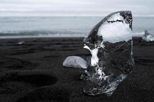 Doorzichtig stuk van glaciaal ijs Aan de zwart zand van diamant strand, IJsland foto