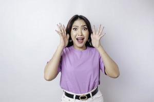 een portret van een geschokt Aziatisch vrouw vervelend een lila Purper t-shirt, geïsoleerd door een wit achtergrond foto