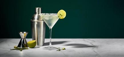 martini glas met cocktail of mocktail en limoen wig, shaker en jigger Aan donker achtergrond foto