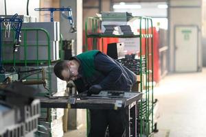 een geüniformeerd arbeider werken in een modern metaal productie en verwerken fabriek assembleert onderdelen van een nieuw machine Aan zijn bureau foto