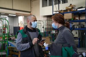 industrieel arbeiders met gezicht maskers beschermde tegen corona virus bespreken over productie in fabriek. mensen werken gedurende covid-19 pandemie. foto