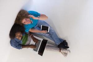 multi-etnisch paar zittend Aan de verdieping met een laptop en tablet top visie foto