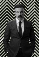 zwart en wit portret van een elegant elegant senior zakenman met een baard en gewoontjes bedrijf kleren tegen retro kleurrijk patroon ontwerp achtergrond gebaren met handen foto