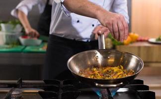 chef zetten specerijen Aan groenten in wok foto