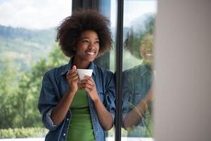 Afrikaanse Amerikaans vrouw drinken koffie op zoek uit de venster foto