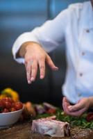 chef zetten zout Aan sappig plak van rauw steak foto