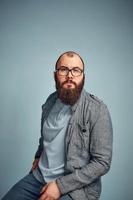 levensstijl geslaagd jong Mens met bril , baard, modieus denim jasje op zoek voorwaarts, mannelijk portret in de studio Aan een uniform achtergrond. foto