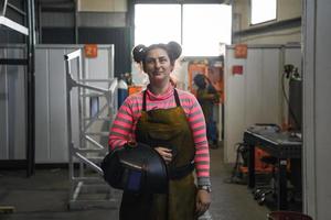 een portret van een Dames lasser Holding een helm en voorbereidingen treffen voor een werken dag in de metaal industrie foto