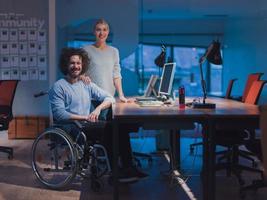 zakenman in een rolstoel in modern coworking kantoor ruimte werken laat nacht in kantoor. collega's in achtergrond. onbekwaamheid en handicap concept. foto