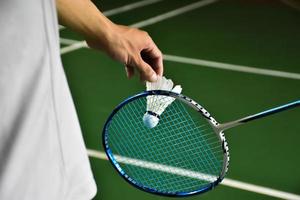 badminton speler houdt racket en wit room shuttle in voorkant van de netto voordat portie het naar een ander kant van de rechtbank. foto