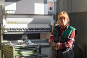 portret van een vrouw staand in voorkant van een cnc machine in stofbril en werken in een modern metaal productie en verwerken fabriek foto