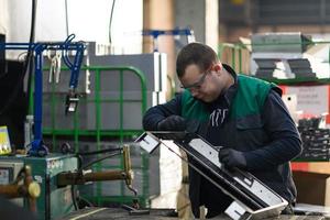 een geüniformeerd arbeider werken in een modern metaal productie en verwerken fabriek assembleert onderdelen van een nieuw machine Aan zijn bureau foto