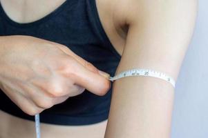 dichtbij omhoog van jong vrouw in sport beha gebruik makend van een meten plakband voor meten haar arm lengte. foto